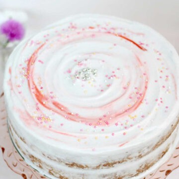 A beautifully iced gluten dairy free vanilla cake. The icing has been swirled with a palette knife and had tones of white and reds. Sprinkles have also been added.