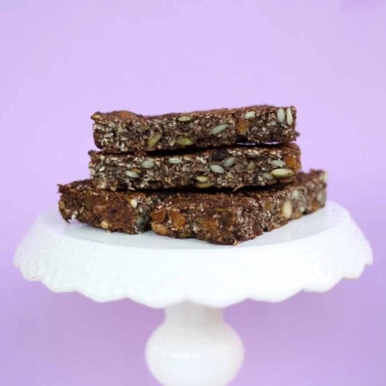 Pieces of yummy granola bars displayed on white cake stand in front of a purple background.