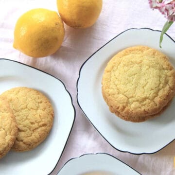 Delicious lemon cookies served on plates. Two lemons and some flowers are in the shot also.