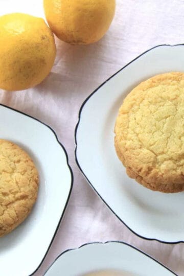Delicious lemon cookies served on plates. Two lemons and some flowers are in the shot also.