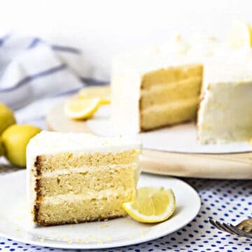 Delectable lemon layer cake served on a plate with the rest of the cake in the background.