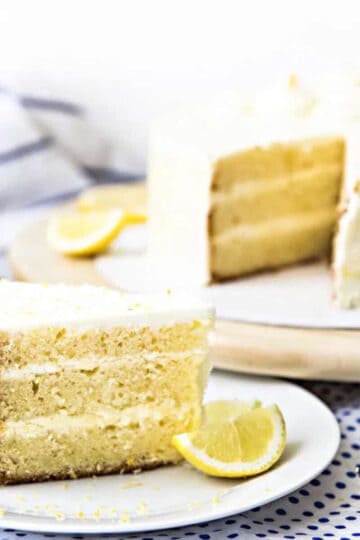 Delectable lemon layer cake served on a plate with the rest of the cake in the background.