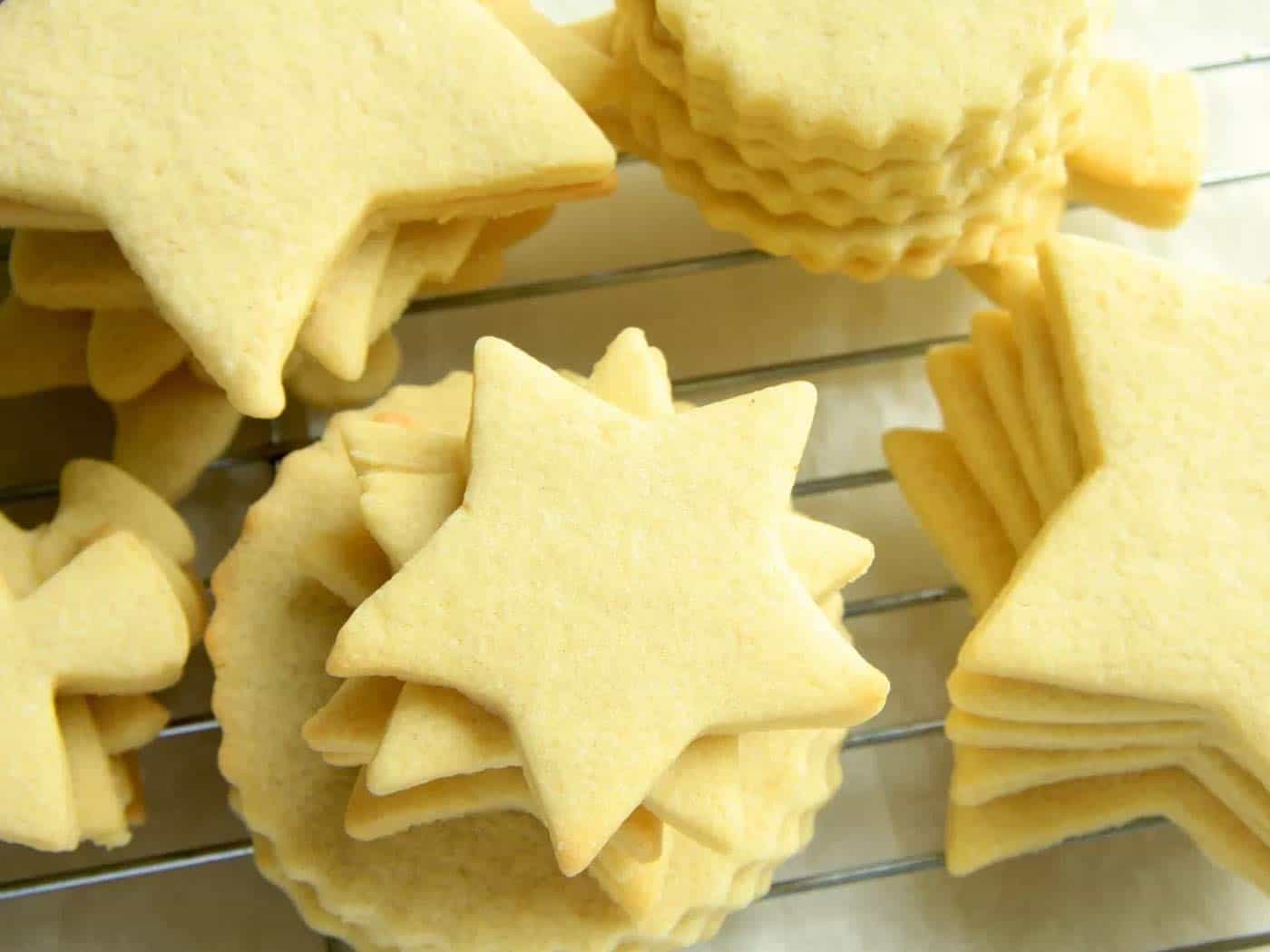Different shapes of sugar cookies stacked on a cooling rack without icing.