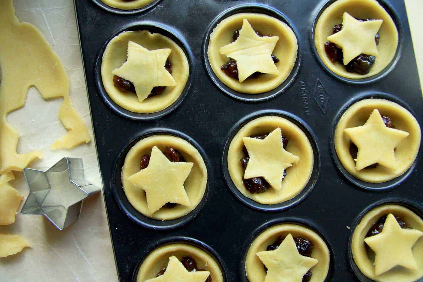 Christmas mince pies in the muffin tin unbaked. A star cookie cutter and pastry rolled out next to it.