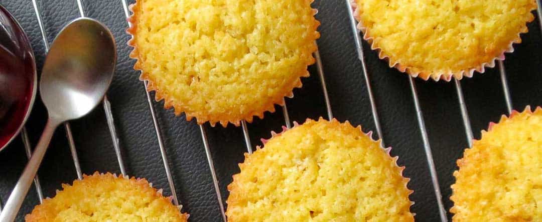 Almond cupcakes before being iced are on a cooling rack.