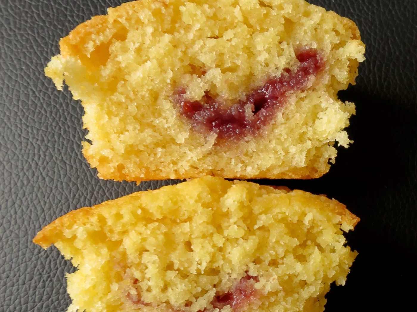 Two cupcakes cut in half. The top one has a fluffy and tender crumb where as the bottom on is more coarse and tough in texture. The jam filling in the middle is dispersed better in the top one.