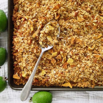 A baking tray with feijoa granola on it with a serving spoon on it ready to scoop into bowls. There are several fresh feijoas on the side of the baking tray.