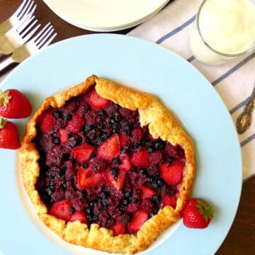 Mixed berry galette on a blue plate with side plates, forks and a jar of cream/yoghurt next to it.