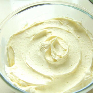 A glass bowl filled with creamy white chocolate buttercream. It has been swirld around the bowl to show how creamy and fluffy it is.