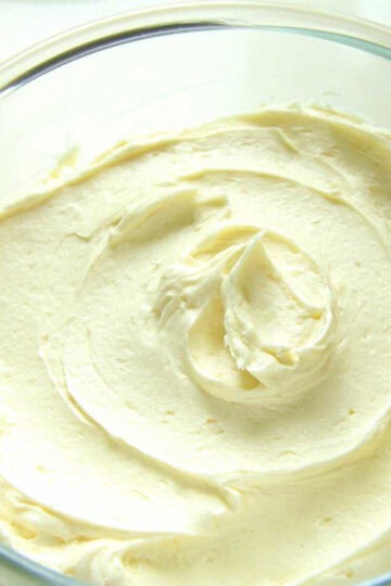 A glass bowl filled with creamy white chocolate buttercream. It has been swirld around the bowl to show how creamy and fluffy it is.