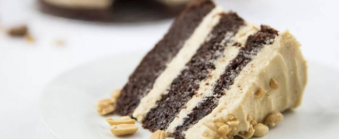 A slice of chocolate layer cake on it's side. It has peanut butter icing in between the layers with chopped nuts on the top.