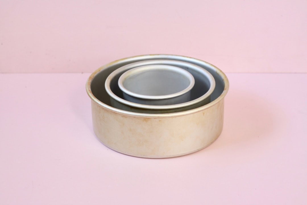 Three different sized cake tins sitting inside of each other. Pink background.