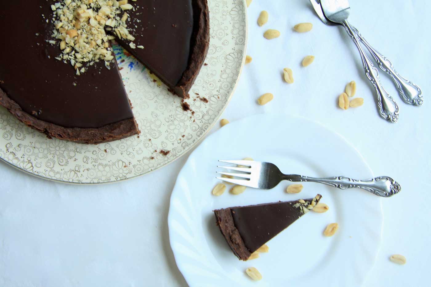 Moorish chocolate tart on a serving plate, with one piece cut and served on a side plate. White table cloth background with forks to the side.