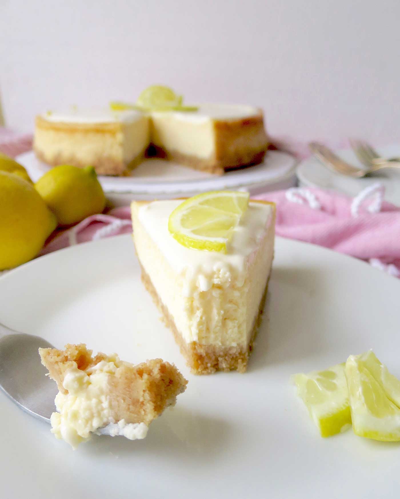 A slice of lemon cheesecake with a fork next to it with a bite sized piece of cheesecake on it, ready to eat.