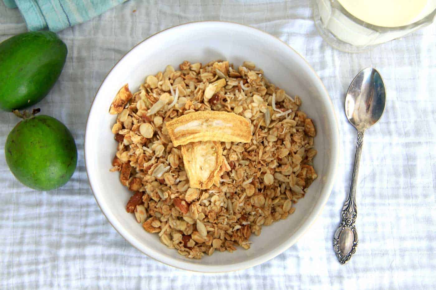 A breakfast bowl of feijoa granola, a spoon on the side and a jug of milk ready to pour into the granola.