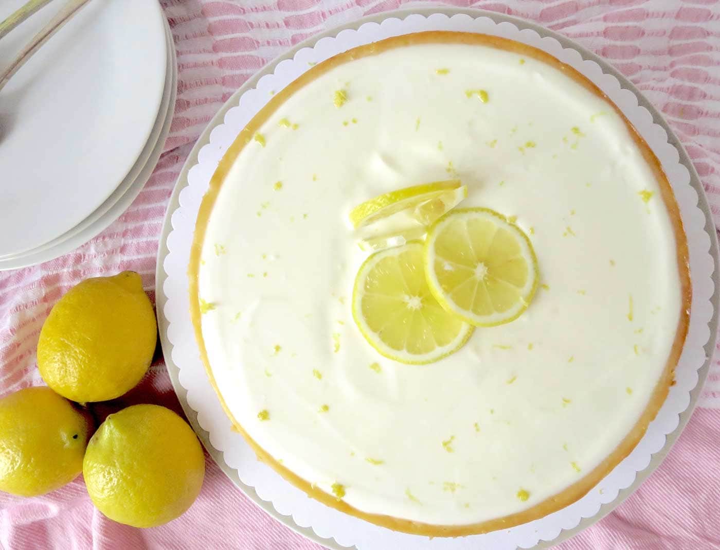 Top view of entire cheesecake. Three lemon slices are placed right in the middle of the cheese cake and lemon zest has been sprinkled on top to decorate the surface area of the cheesecake.
