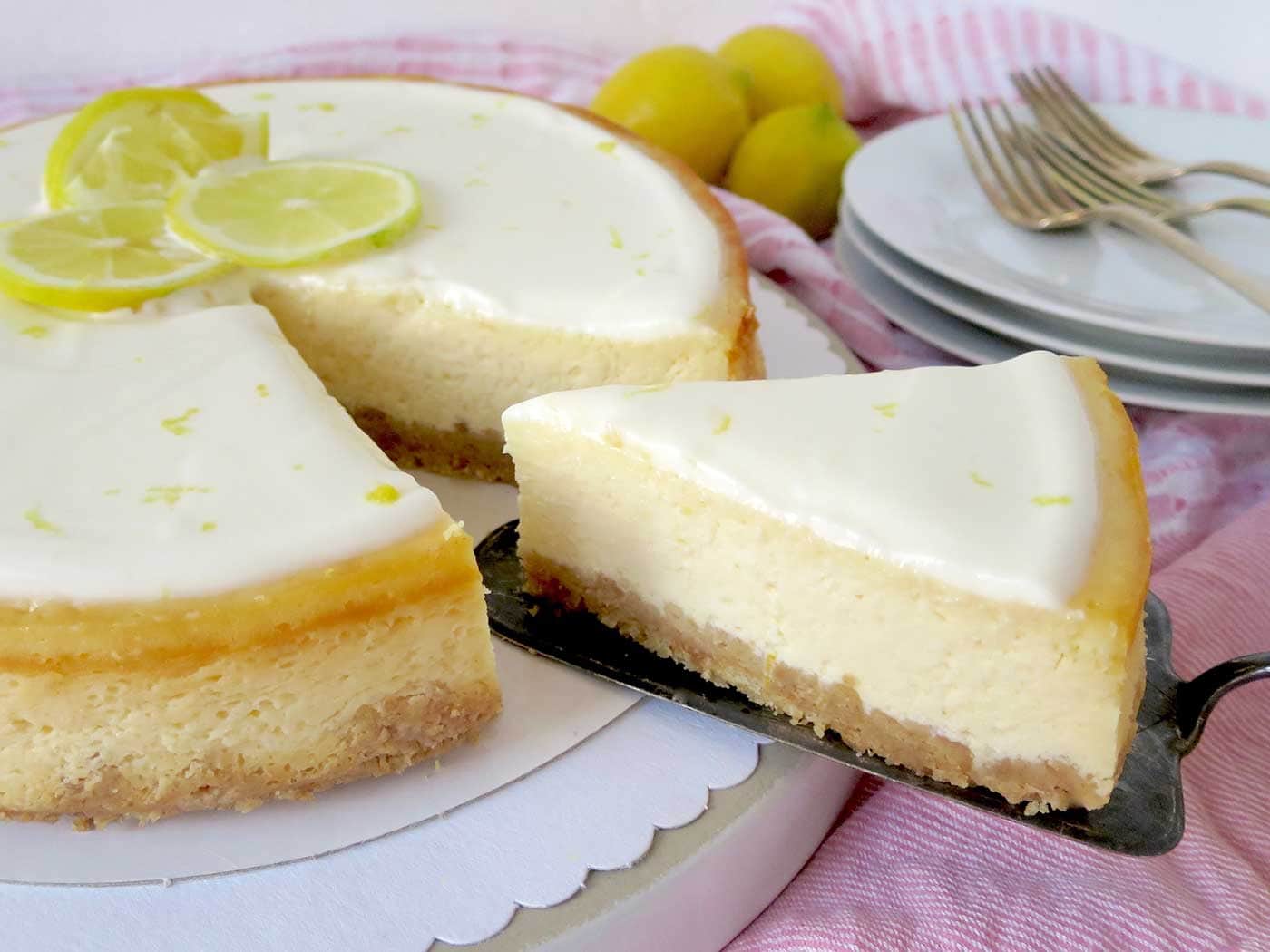 A close up shot of the side of cheesecake slice. Showcasing a thick biscuit base and luscious lemon cream cheese filling and sour cream layer.