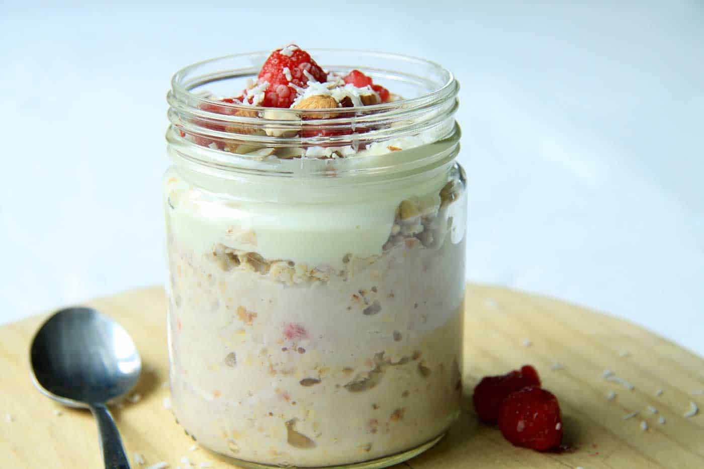 Raspberry coconut oats in a glass jar sitting on a board.
