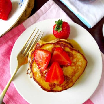 Birds eye view of a a stack of strawberry buttermilk pancakes topped with freshly sliced strawberries and a generous lathering of maple syrup.
