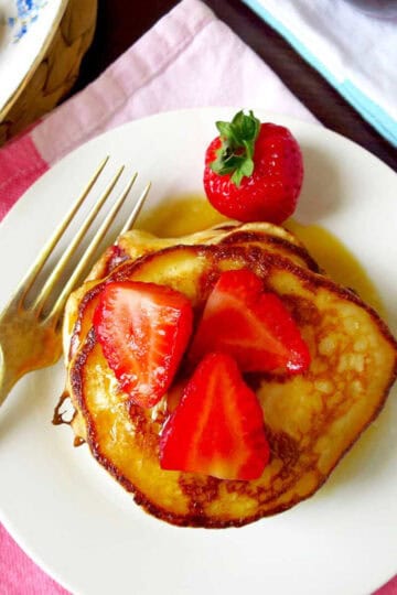 Birds eye view of a a stack of strawberry buttermilk pancakes topped with freshly sliced strawberries and a generous lathering of maple syrup.