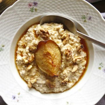 A vintage bowl filled with a creamy vanilla porridge. It's topped with a maple roast pear quarter and it has roasted walnuts sprinkled around it.