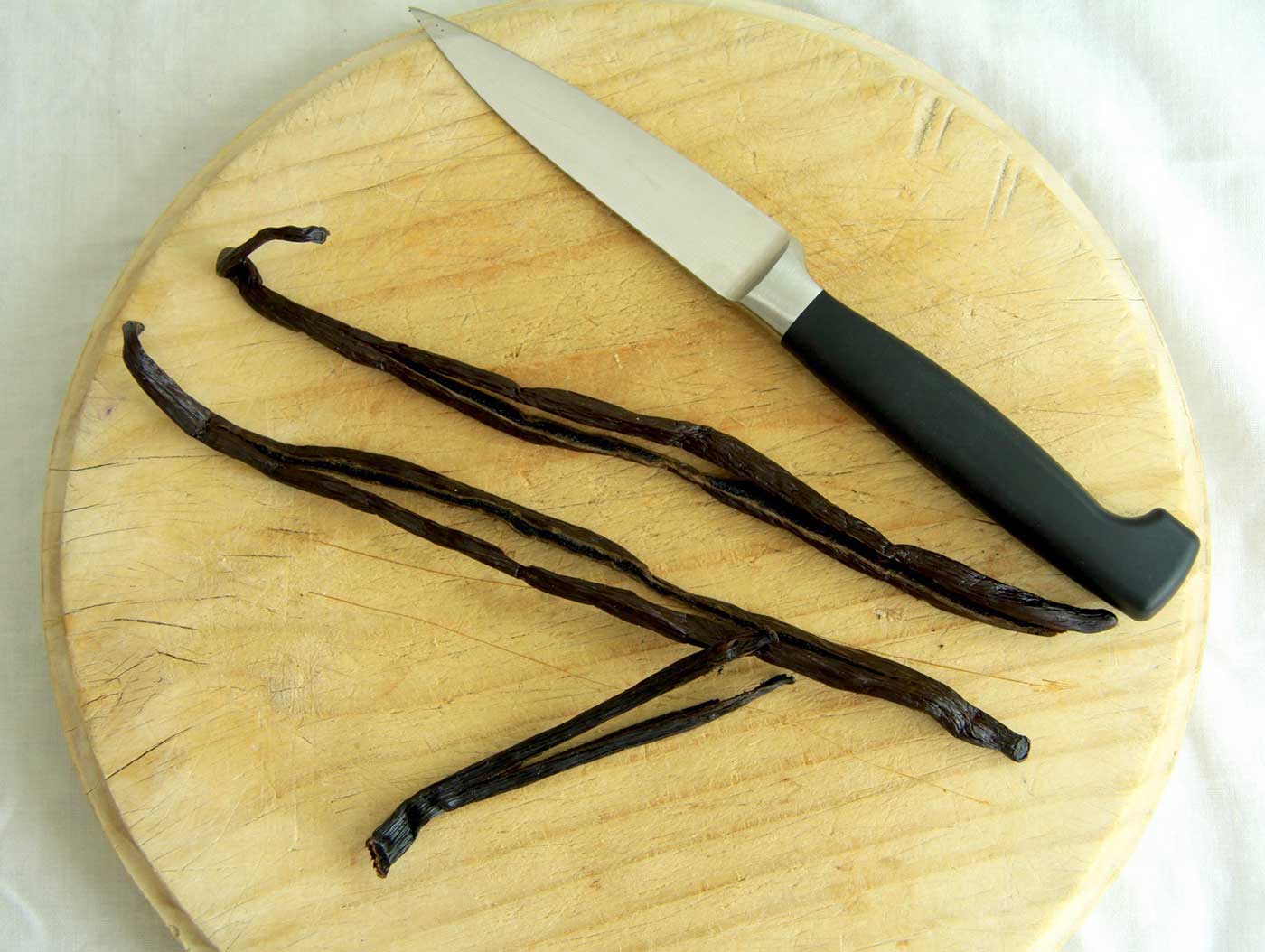 Vanilla pods on a chopping board with a knife next to them, ready for slicing the pods open.
