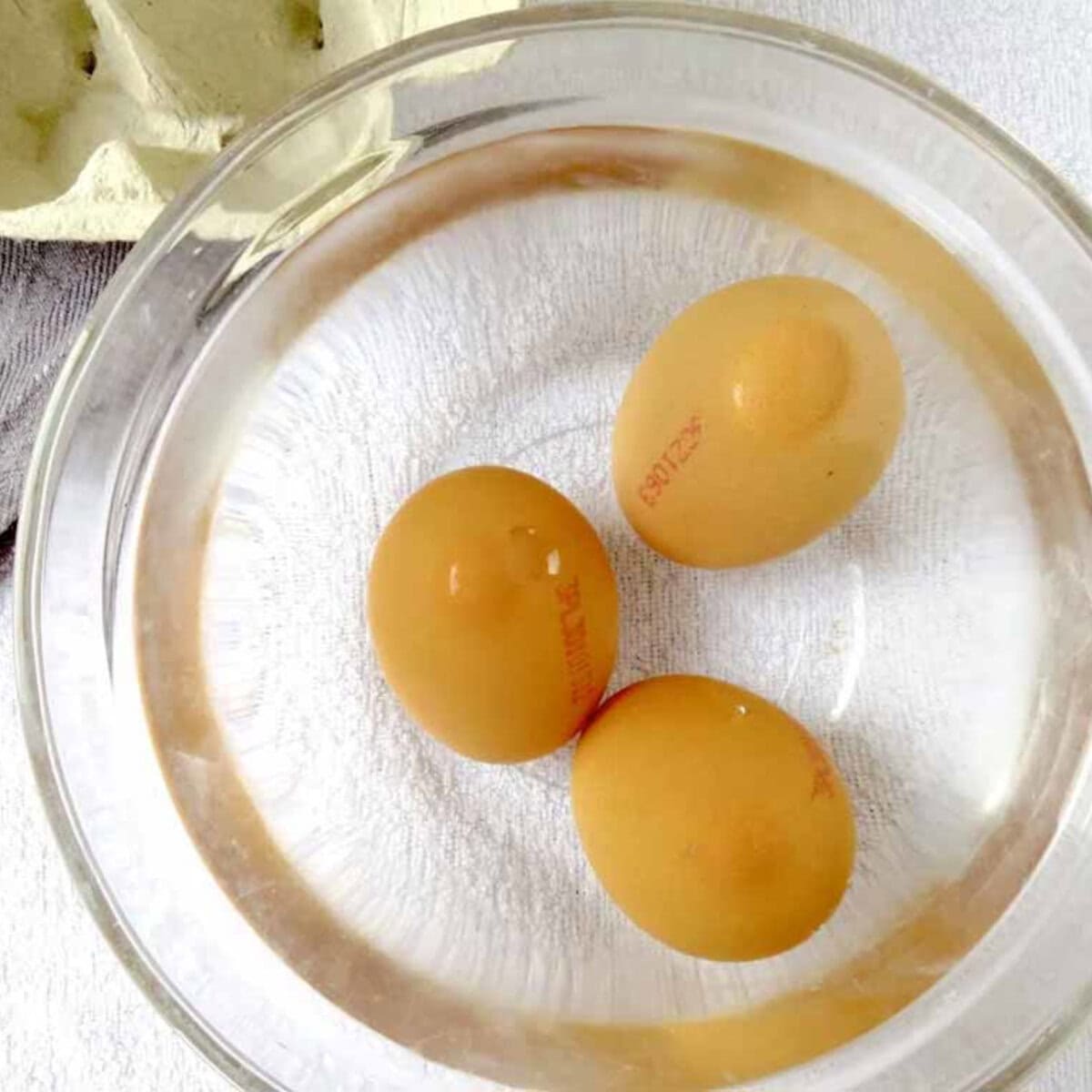 Three eggs in a glass bowl of water.