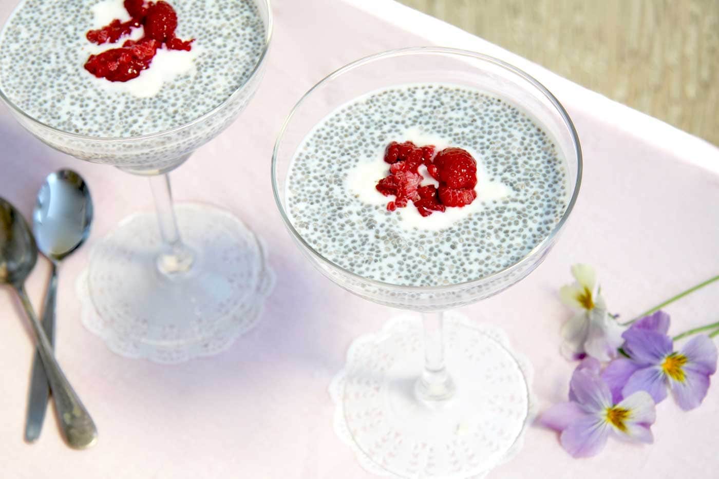 Top view of chia seed puddings in margarita glasses. Both puddings are topped with cooked rasbperries and a dollop of yoghurt.