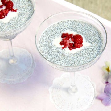 Two margarita glasses filled with chia seed pudding on a pink table. There is berry compote and yoghurt in the middle of each glass to decorate.