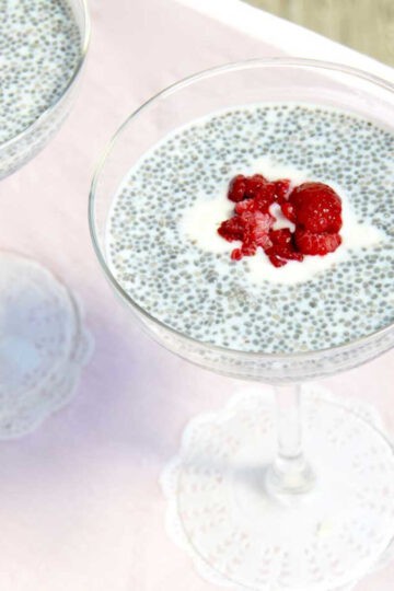 Two margarita glasses filled with chia seed pudding on a pink table. There is berry compote and yoghurt in the middle of each glass to decorate.