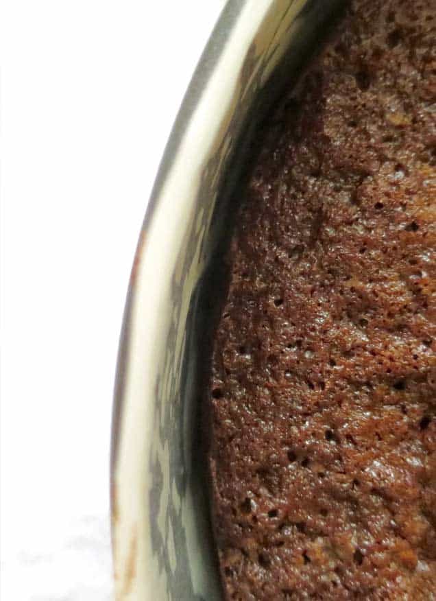 A baked chocolate cake in a tin with a close up shot of the baked chocolate cake coming away from the side of the tin.