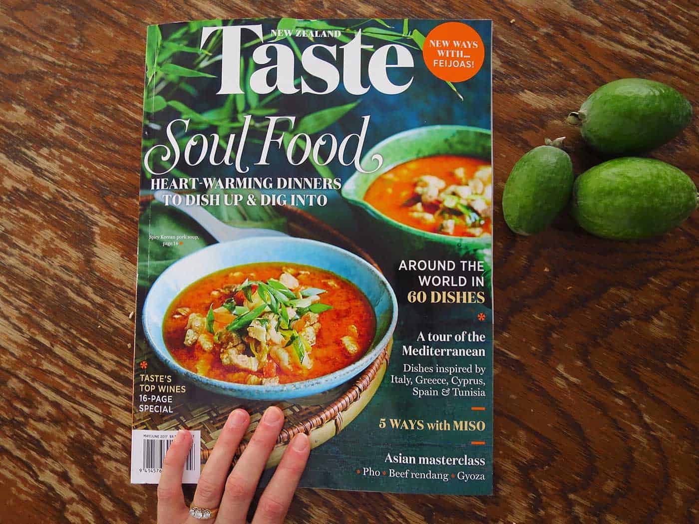 A hand holding a copy of the Taste magazine cover, ready to open