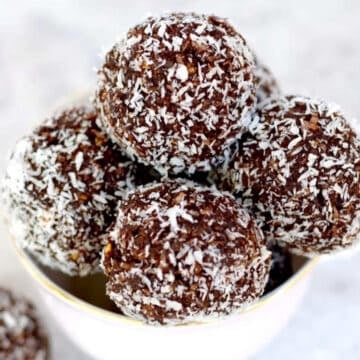 Chocolate vegan bliss balls in a pink tea cup which have been rolled in coconut.