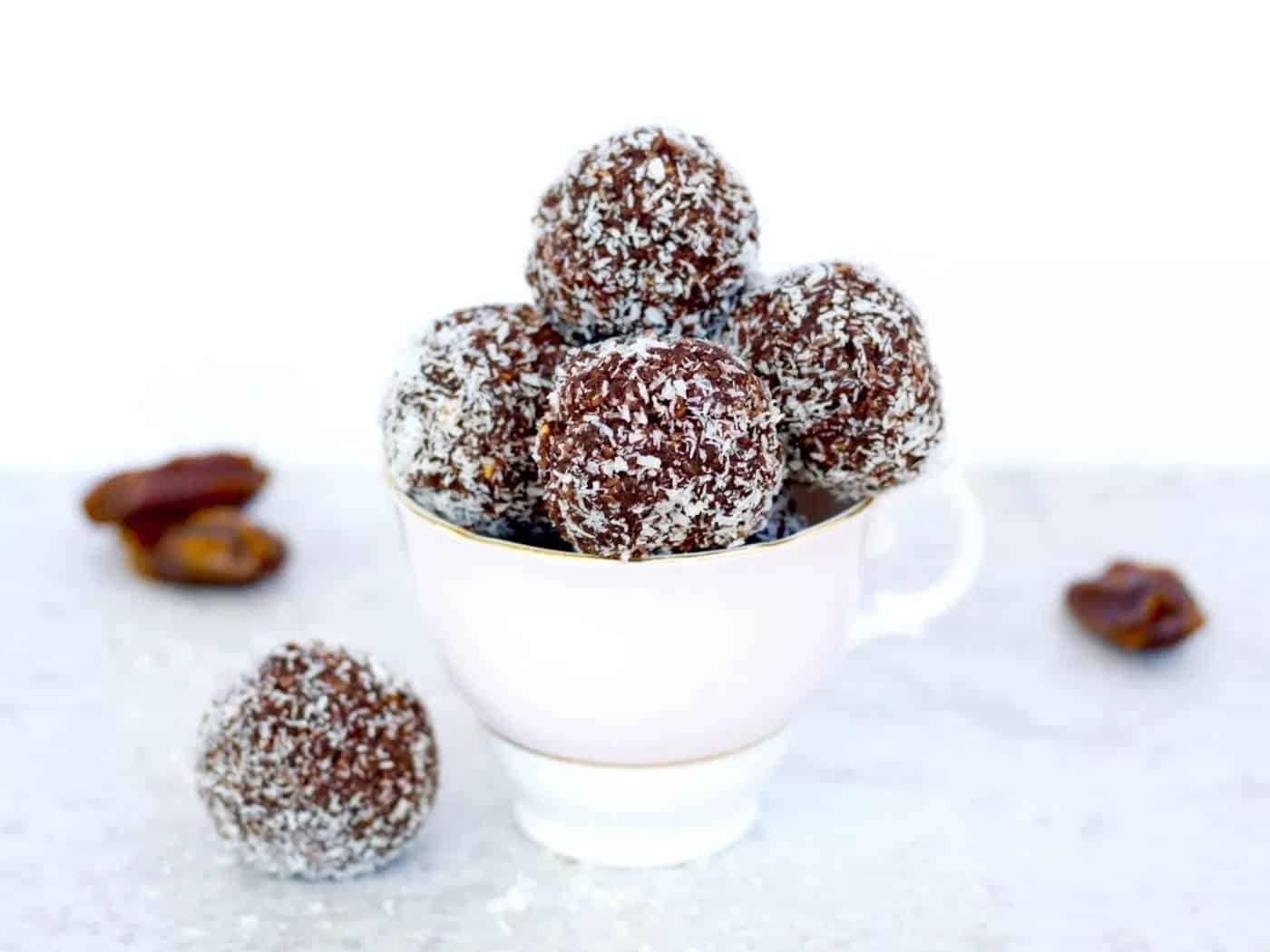 A vintage teacup filled with chocolate bliss balls and one on the side. Dates on the side also.
