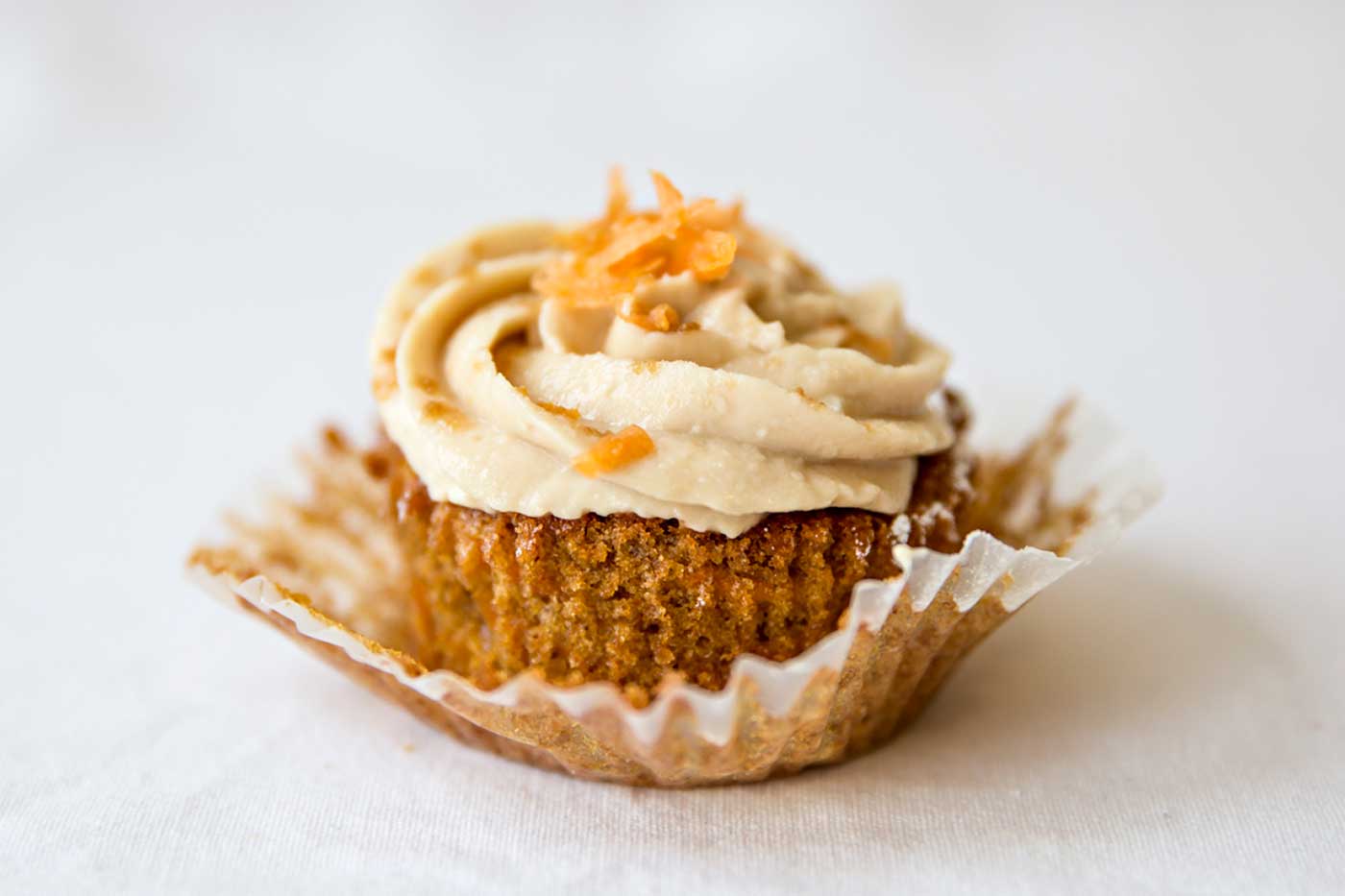 One carrot cupcake with brown sugar cream cheese frosting with wrapper peeled back.
