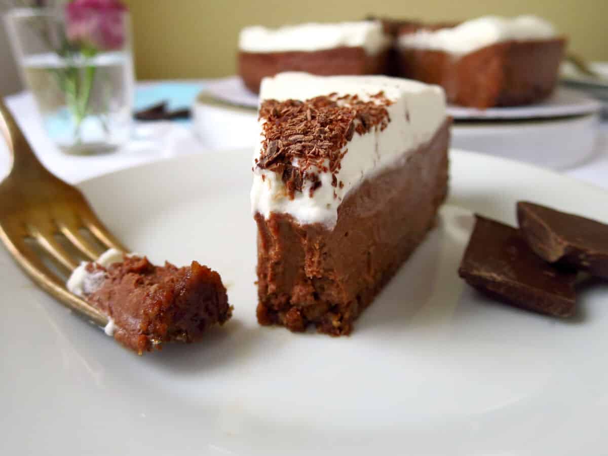 A piece of chocolate cheesecake with a fork which has a bite size piece ready to eat.