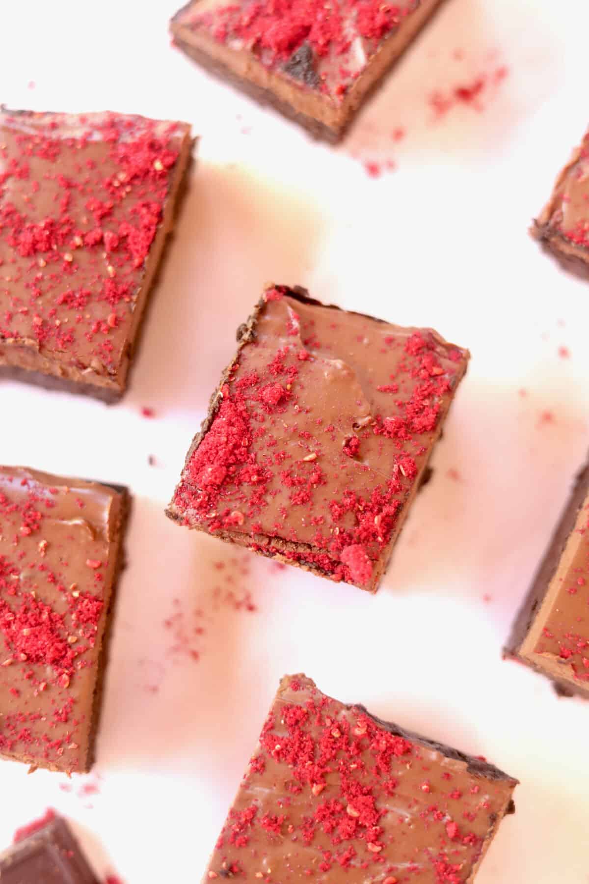 Several pieces of delicious and decadent chocolate vegan brownies on a white board. Berry powder is dusted all over.