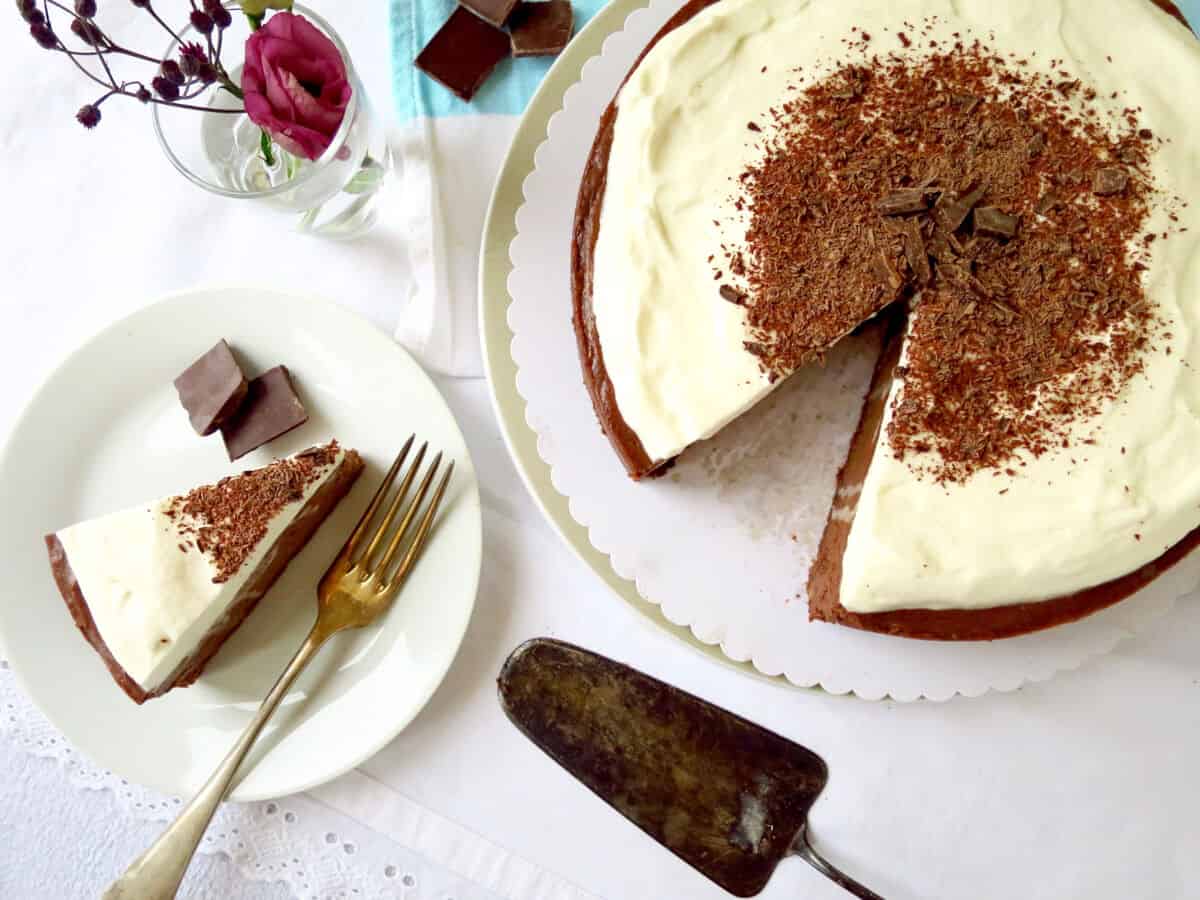 A velvet chocolate cheesecake with a creamy topping and chocolate shards sprinkled on the top. A slice has been cut and served on the plate next to it.