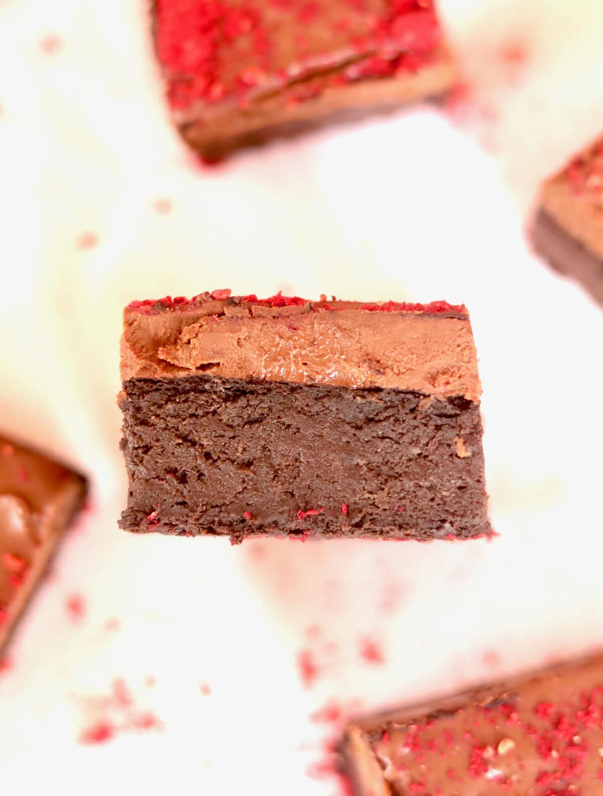 A side view of a piece chocolate vegan brownie with other pieces in the background.