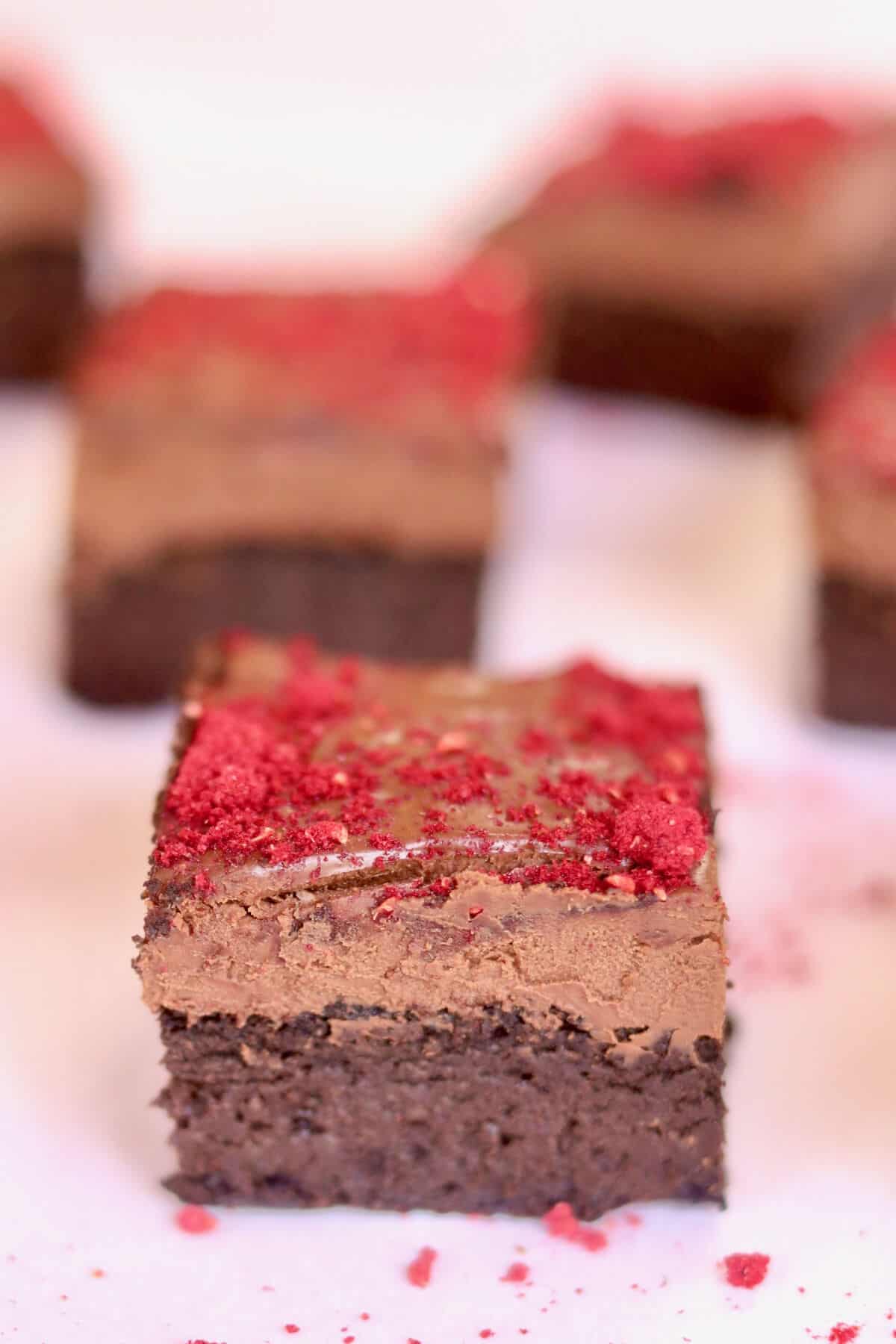 A close up of a piece of vegan chocolate brownie with other pieces behind it in the background.