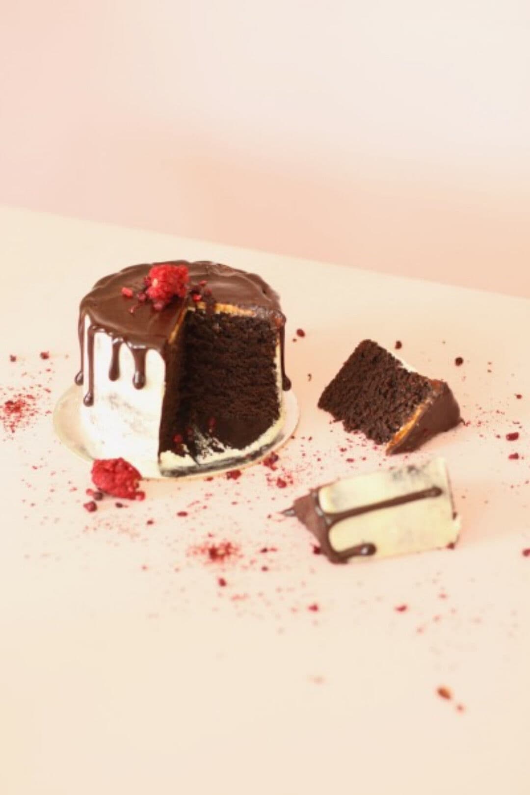 A rich chocolate cake which has been cut into a couple of slices. It has gorgeous chocolate drizzle on the top running down the sides and freeze dried berries sprinkled on the top.