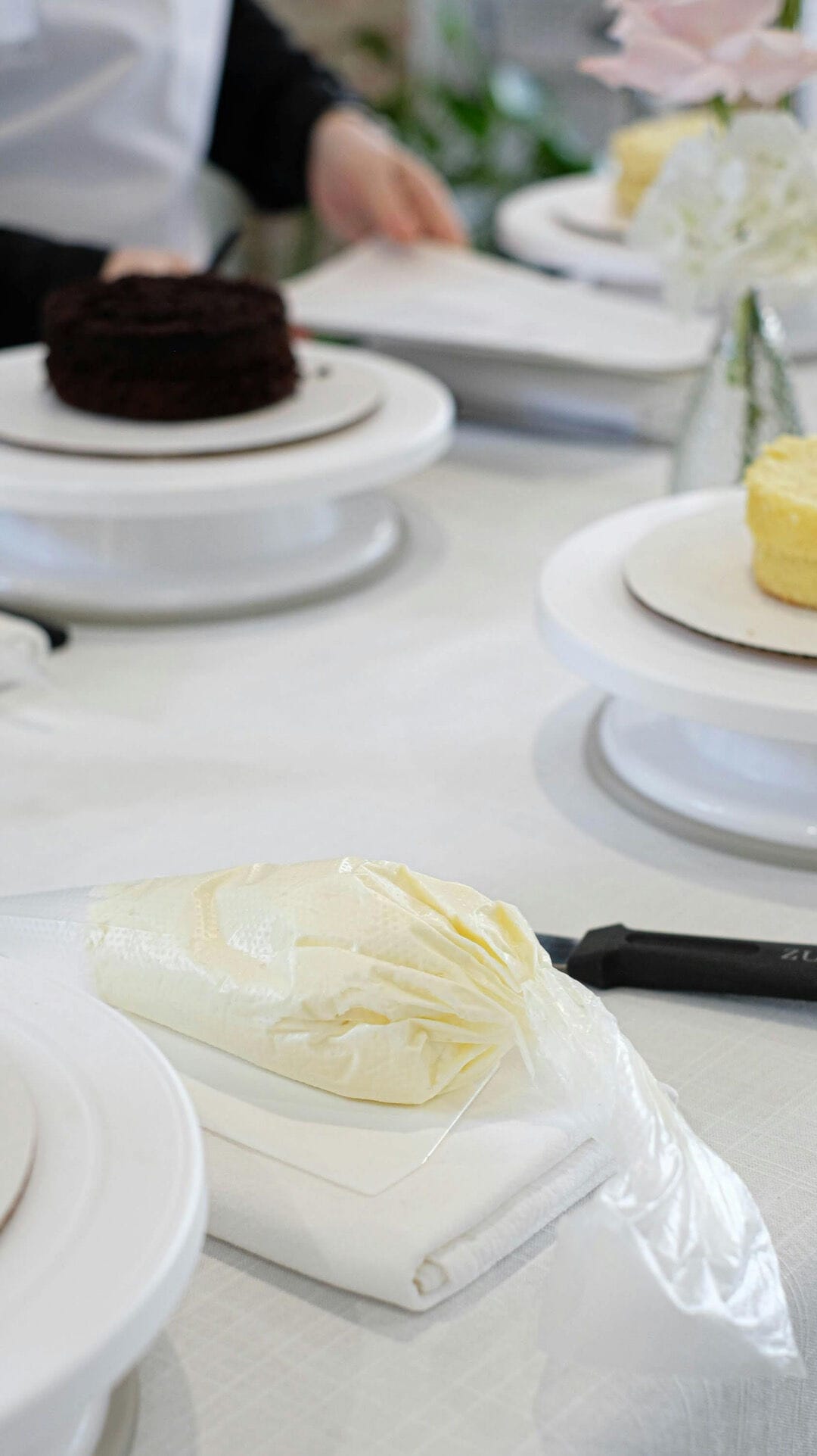 Buttercream in a piping bag ready to frost a cake. A person nearby by with a chocolate cake ready to be frosted.