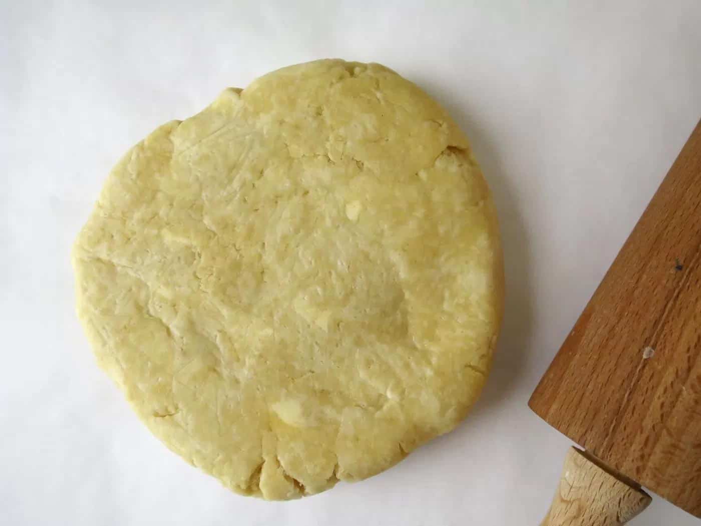 A disc of homemade buttermilk pastry which has been rolled out slightly. A wooden rolling pin is next to it.