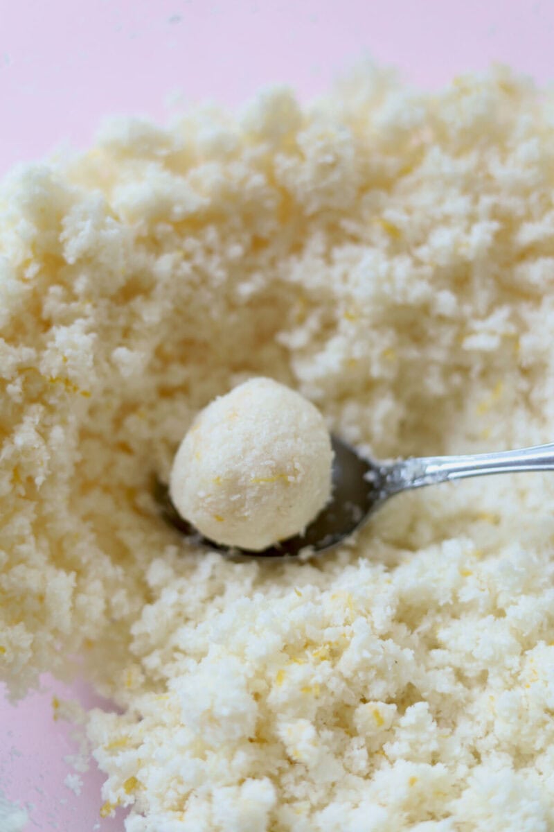 A bowl of lemon coconut mixture with a spoon. A portion of mixture has been rolled into a walnut size ball.