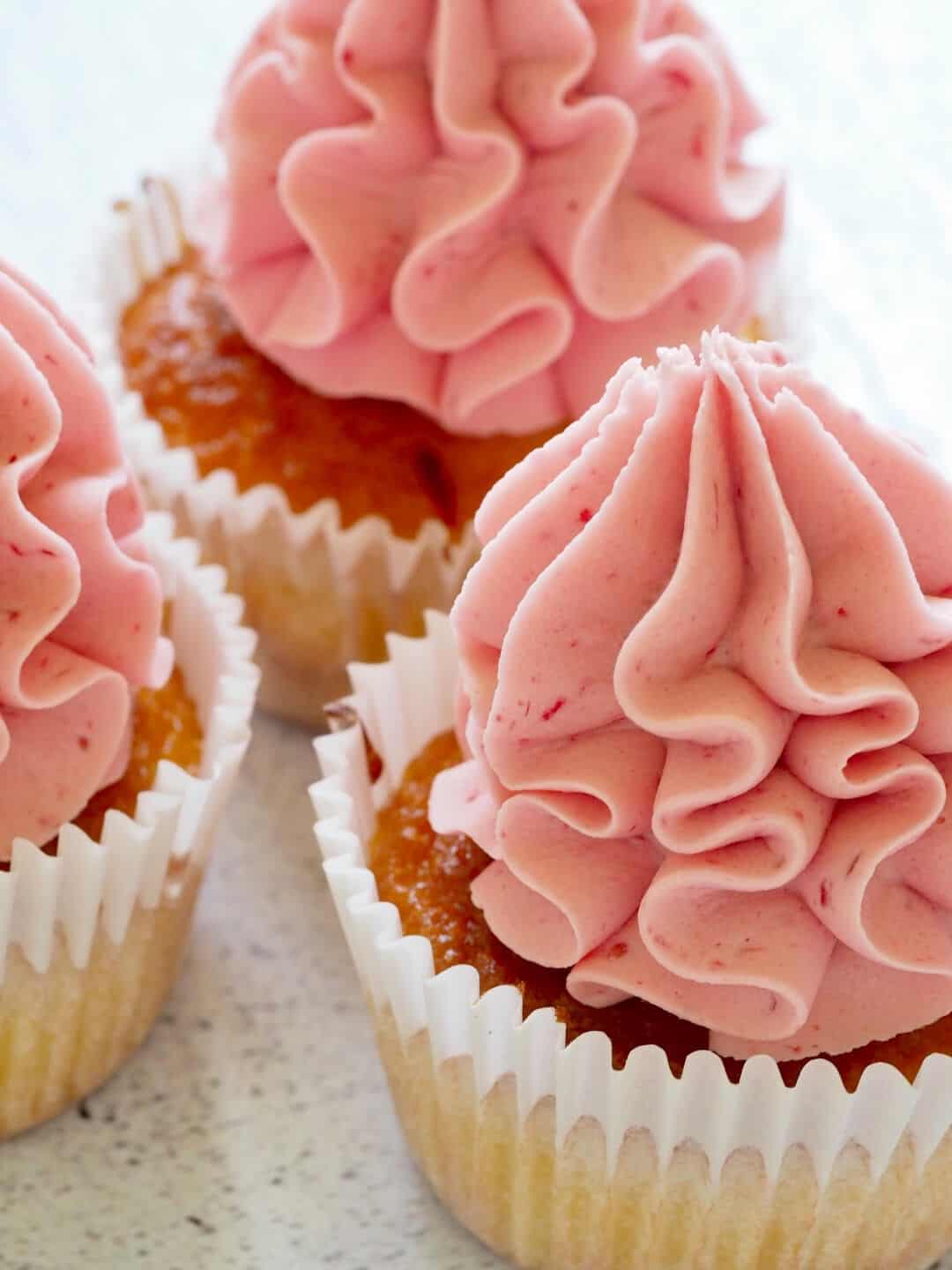Several vanilla cupcakes topped with frilly raspberry buttercream.