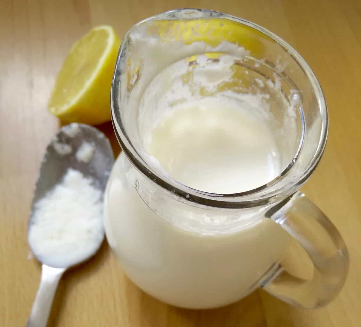 A jug of homemade buttermilk with some lemon on the side and a spoon with buttermilk on it. Perfect for creating flaky pastry!