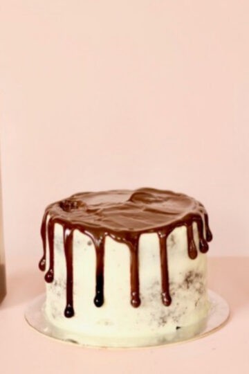 A cake topped with a delicious chocolate drizzle and a drizzle bottle and glass bowl with left over ganache inside it.