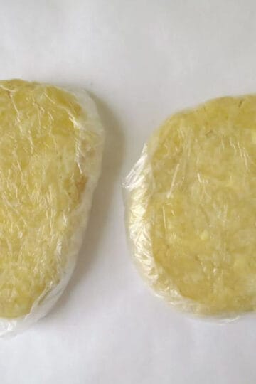 Two discs of homemade pastry wrapped in plastic wrap and ready to use.