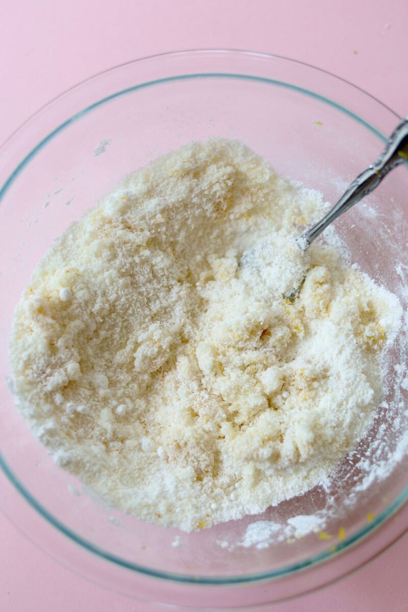 Lemon coconut truffle mixture in a glass bowl with a spoon which has been mixed together.