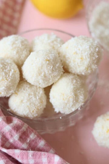 A small glass bowl overflowing with lemon coconut truffles, ready to eat.